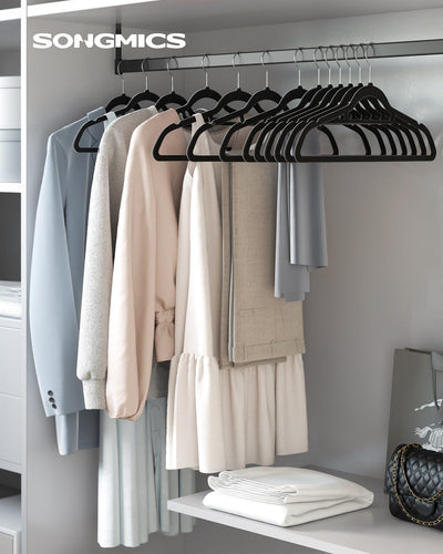 Black velvet hangers holding shirts, trousers and a dress on a wardrobe rail