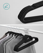 Close-up of stacked black velvet hangers next to hangers loaded with jumpers on a rail
