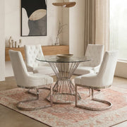 Clear glass round dining table with silver hourglass base in a bright interior