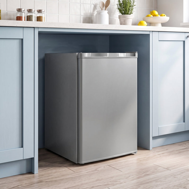 Grey mini freezer set under a kitchen counter between blue cabinets