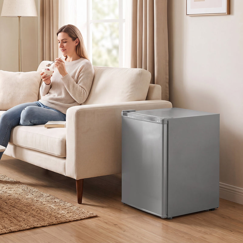 Grey mini freezer next to a sofa while a woman eats ice cream