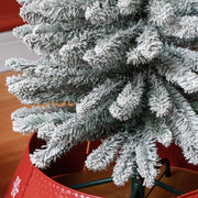 Close-up of snowy branch tips above a red tree skirt and the green metal stand