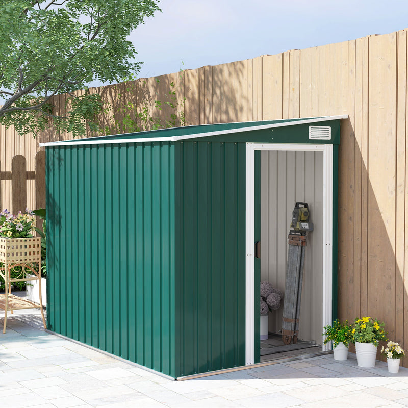 Green lean to metal shed standing against a timber fence with the end sliding door open, showing tools stored inside