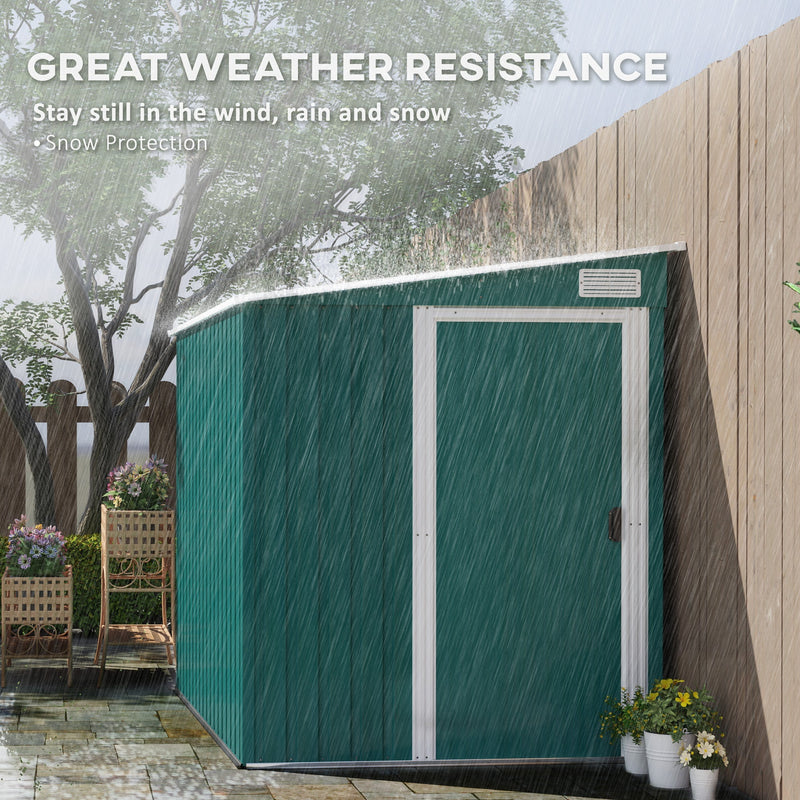 The green lean to shed standing in heavy rain beside a fence, showing its weather resistant panels and sloping roof