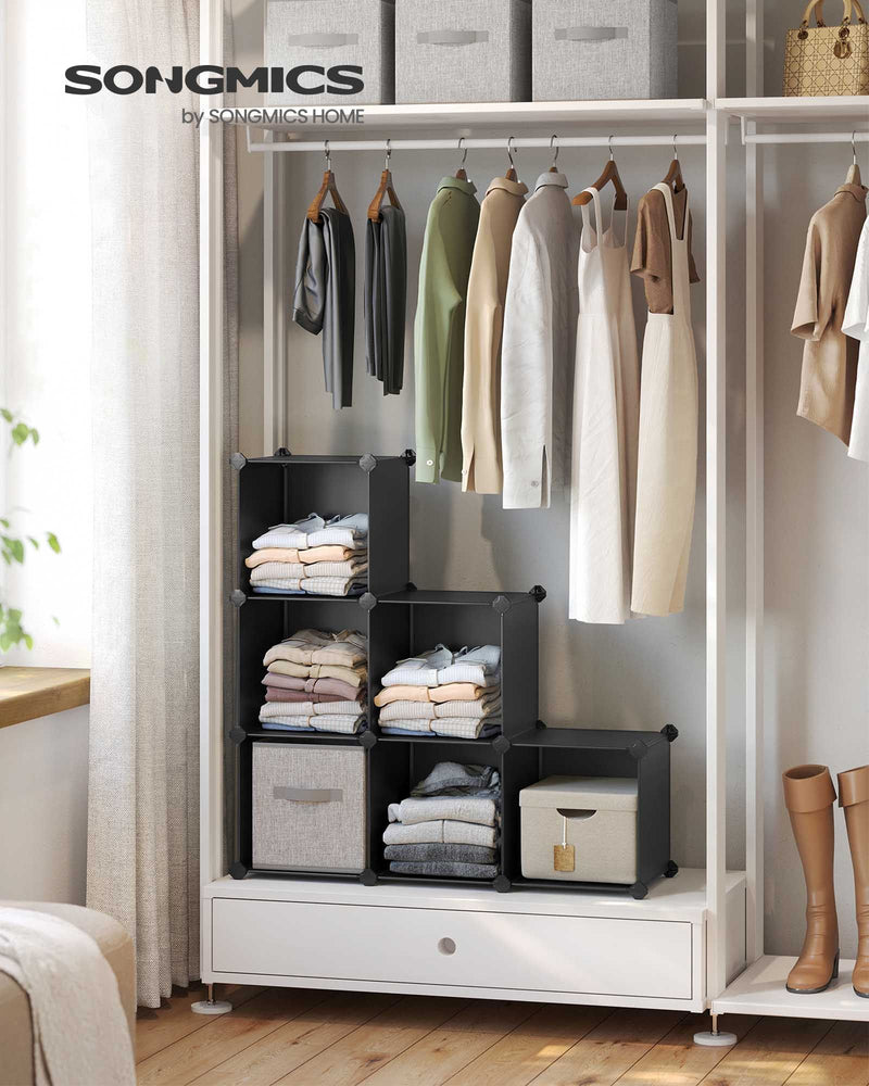 Black cube storage unit in a wardrobe holding folded clothes and fabric bins