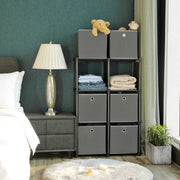 Unit standing beside a bed in a teal bedroom, holding folded clothes and grey boxes with two boxes on top