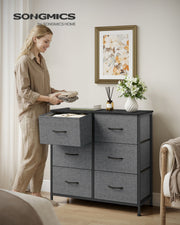 Woman placing folded clothes in an open drawer of the 6-drawer chest in a bedroom