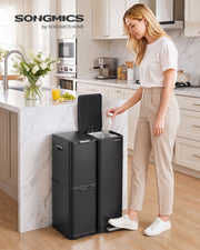 Woman dropping a bottle into the black three-compartment recycling bin in a kitchen