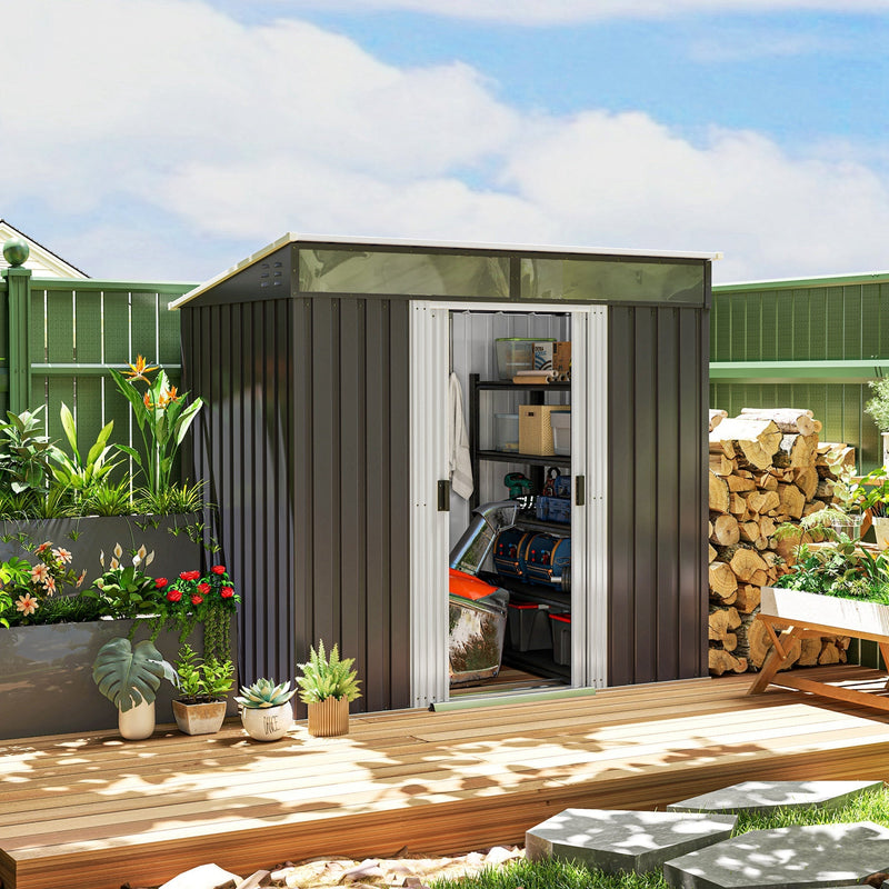 The grey metal shed on decking with its sliding doors open, showing boxes and equipment stored inside