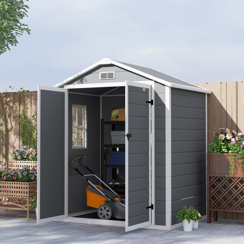 Grey plastic shed on a patio with one door open, a mower and shelves inside
