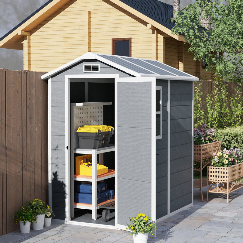 Plastic garden shed beside a timber cabin with the door open showing shelves of tools