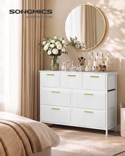 White 7-drawer corduroy chest of drawers in a bedroom with flowers and a round mirror