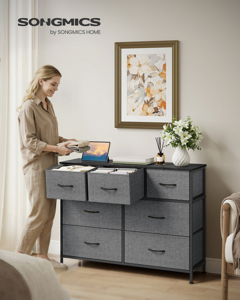 Woman with an open drawer on the slate grey chest of drawers in a bedroom