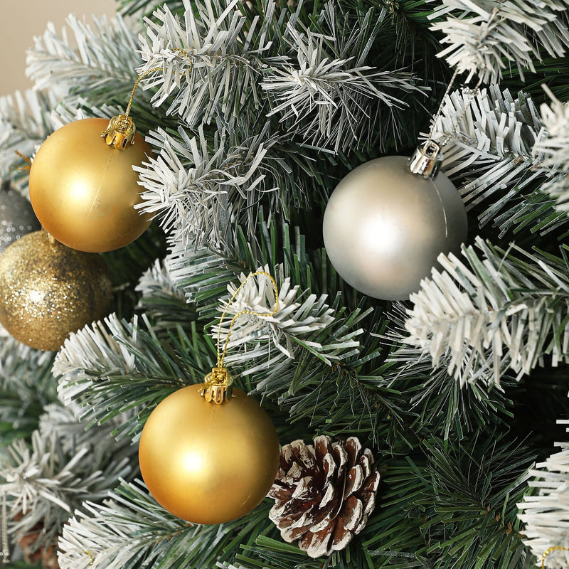 Close-up of gold and silver baubles and a pine cone on snowy branches