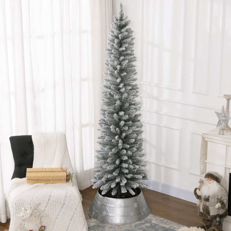 Tall snowy pencil Christmas tree in a silver tree skirt beside an armchair in a bright room