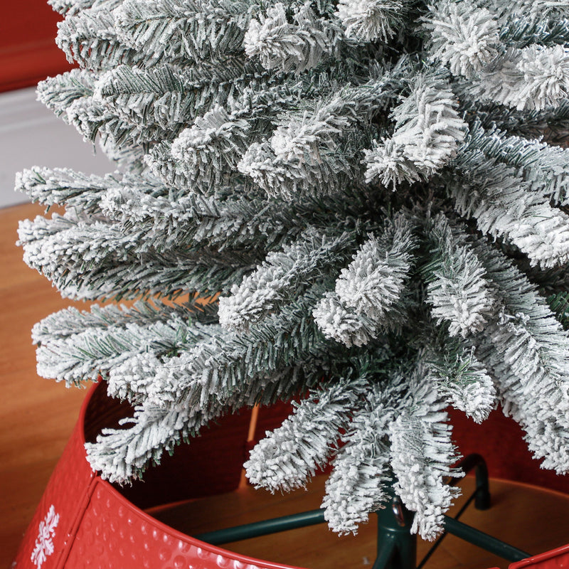 Close-up of snowy branch tips above a red tree skirt and the green metal stand