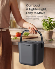 Person carrying the grey compost bin by its handle in a kitchen