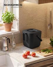 Songmics compost bin on a kitchen counter beside fresh tomatoes and basil