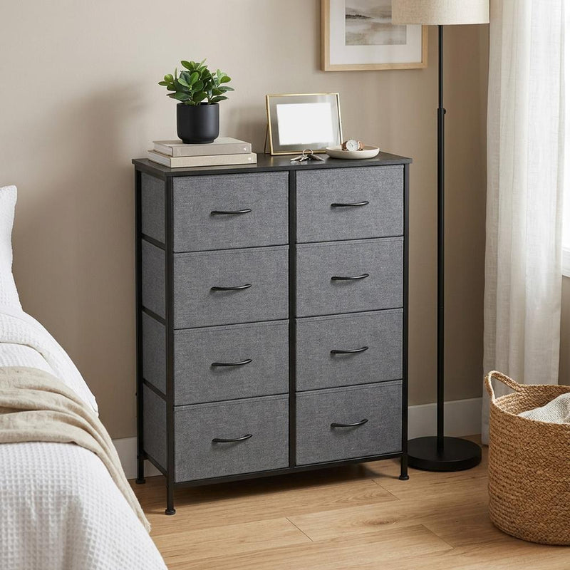 Slate grey chest of drawers beside a bed with a floor lamp and woven basket