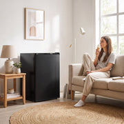 Black mini freezer next to a sofa while a woman eats ice cream