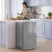 Grey mini freezer beside a kitchen worktop while a woman prepares food