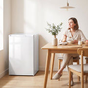White mini freezer beside a dining table while a woman has breakfast