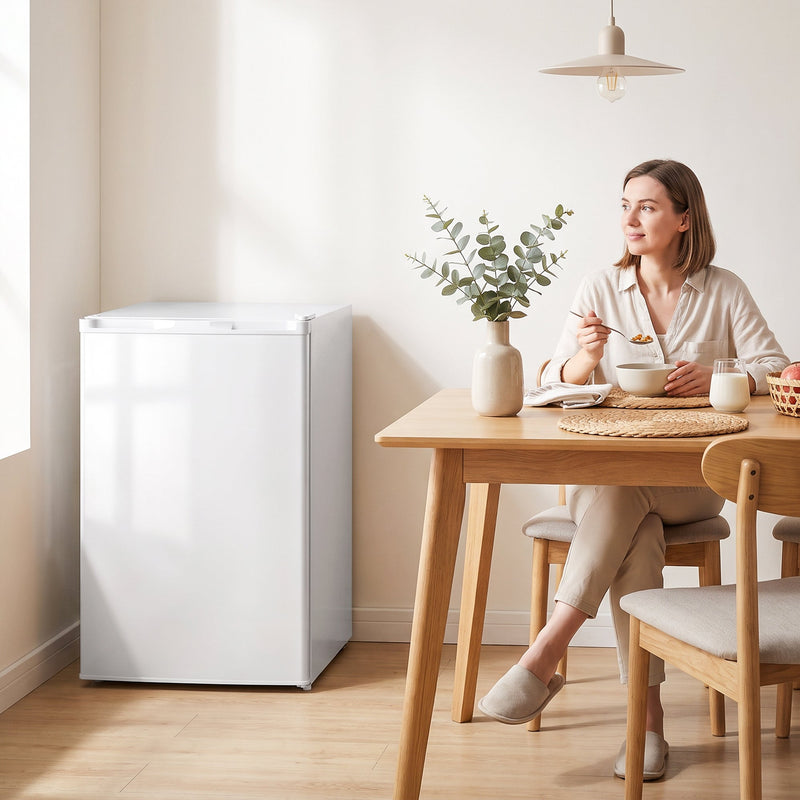 White mini freezer beside a dining table while a woman has breakfast