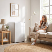 White mini freezer next to a sofa while a woman eats ice cream