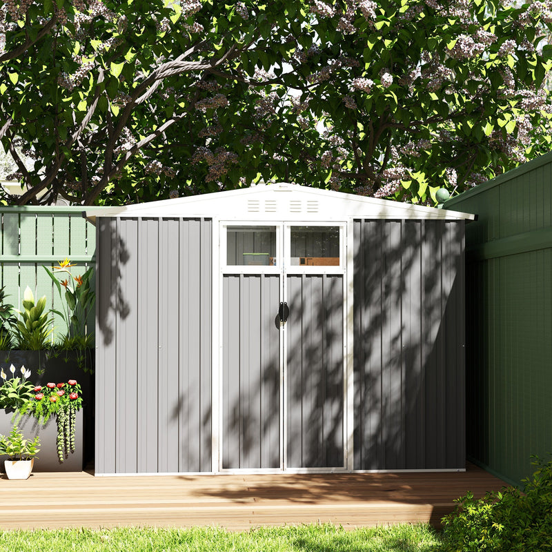Light grey shed closed on garden decking against a dark green fence in dappled sunlight