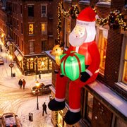 Lit inflatable Santa perched on a window ledge above a snowy street at night