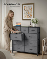 Woman placing folded clothes in an open drawer of the 9-drawer chest in a bedroom