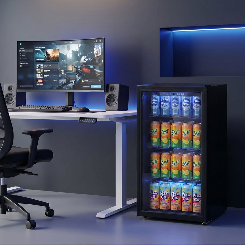 Drinks fridge stocked with cans beside a gaming desk and monitor