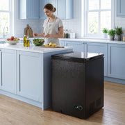 Black chest freezer beside a kitchen island while a woman prepares a salad