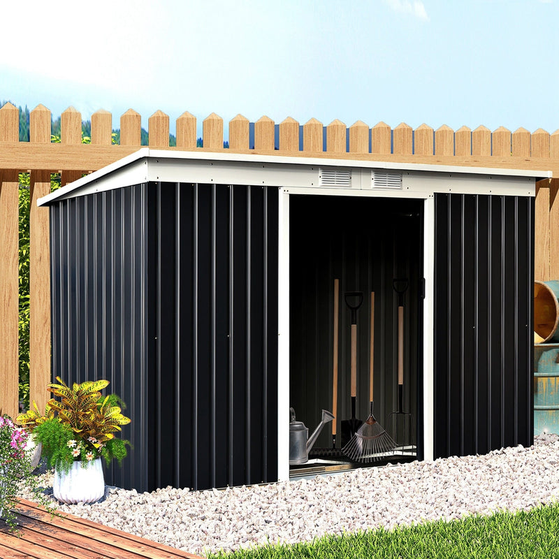 The wide grey shed set against a wooden fence with its sliding doors open, showing rakes and garden tools inside