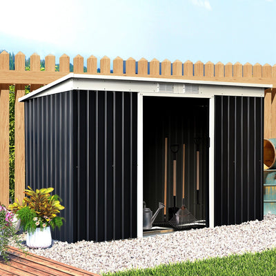 The wide grey shed set against a wooden fence with its sliding doors open, showing rakes and garden tools inside