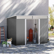 Grey metal shed against a rendered house wall with the sliding doors open, a gas bottle and garden tools inside