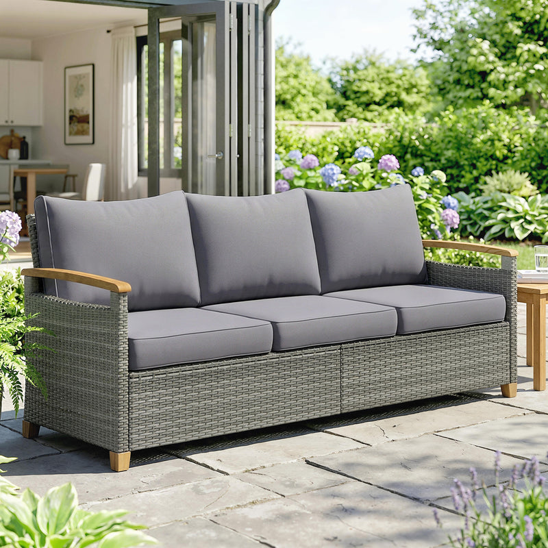 Gray outdoor sofa with cushions on a patio area with greenery and flowers.