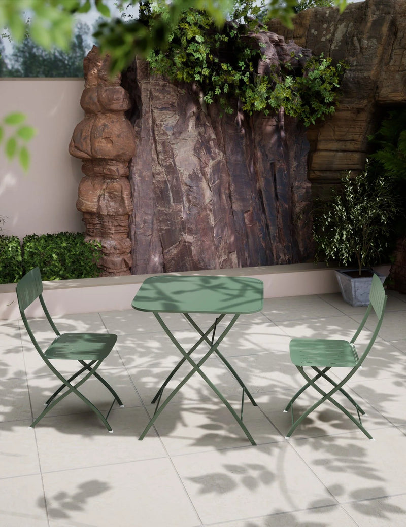 Green metal outdoor table and chairs in a garden setting with rocks and plants.