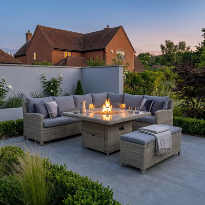 Royalcraft Wentworth rattan corner fire pit set lit at dusk on a garden patio