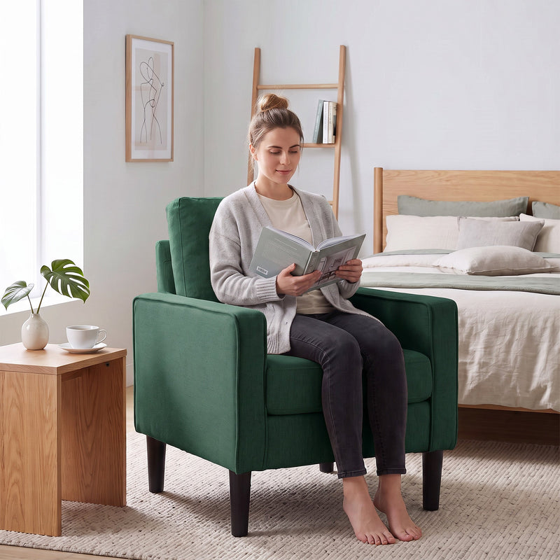 Woman reading a book in the dark green accent chair beside a bed