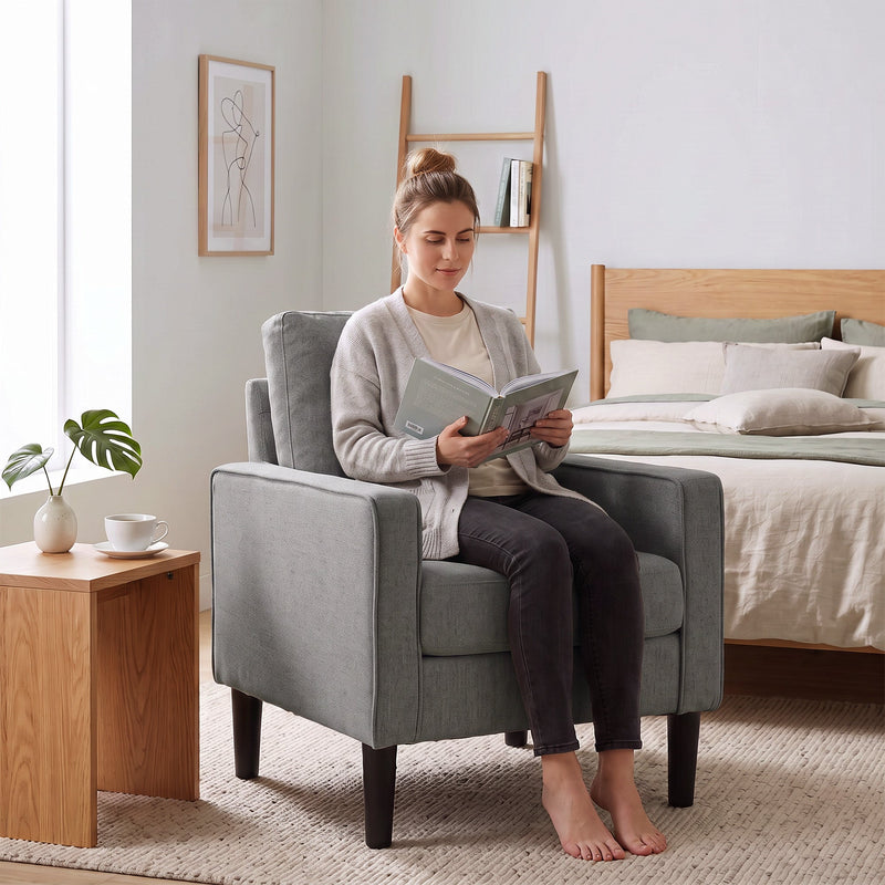 Woman reading a book in the dark grey accent chair beside a bed