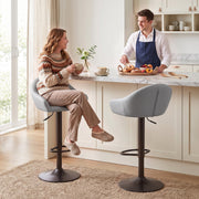 Couple seated on two grey bar stools at a cream kitchen island with coffee and pastries