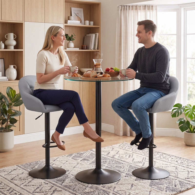 Two grey bar stools at a round glass bar table in a living space with houseplants