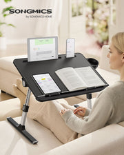 Woman on a sofa using the black laptop desk with a tablet, phone and open book