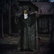 Skeleton reaper decoration lit up at night outside a derelict house
