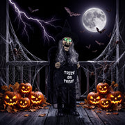 Animated witch decoration with glowing green eyes on a porch surrounded by pumpkins