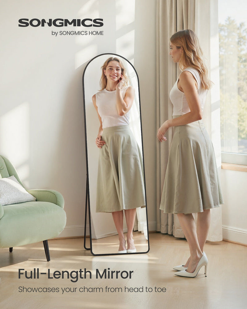 Woman in a white top and green skirt viewing her full-length reflection beside a green armchair