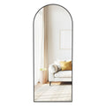 Ink black arched full length mirror on its stand reflecting a living room sofa