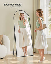 Woman checking her outfit in the ink black arched floor mirror in a bright room