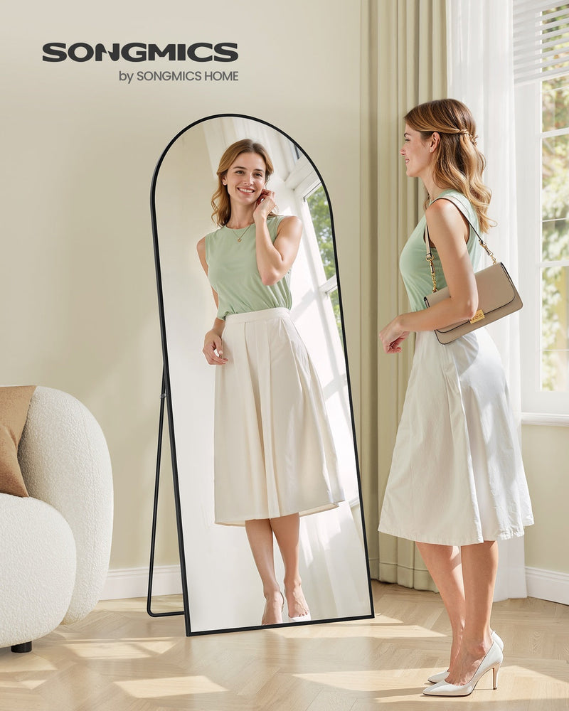 Woman checking her outfit in the ink black arched floor mirror in a bright room